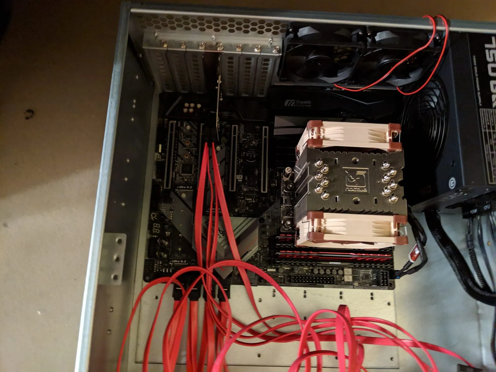 The inside of an open rackmount server chassis with an ASRock X399 board, a large Noctua cooler, and red SATA cables running to drive bays