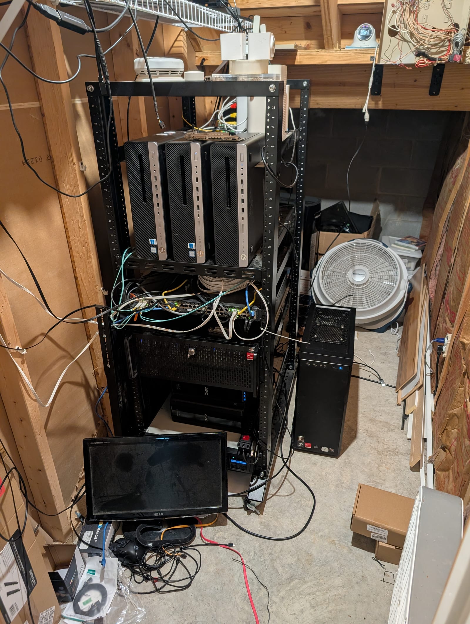 The homelab rack in a basement corner: a 4U EPYC node, three small form-factor machines, and a switch